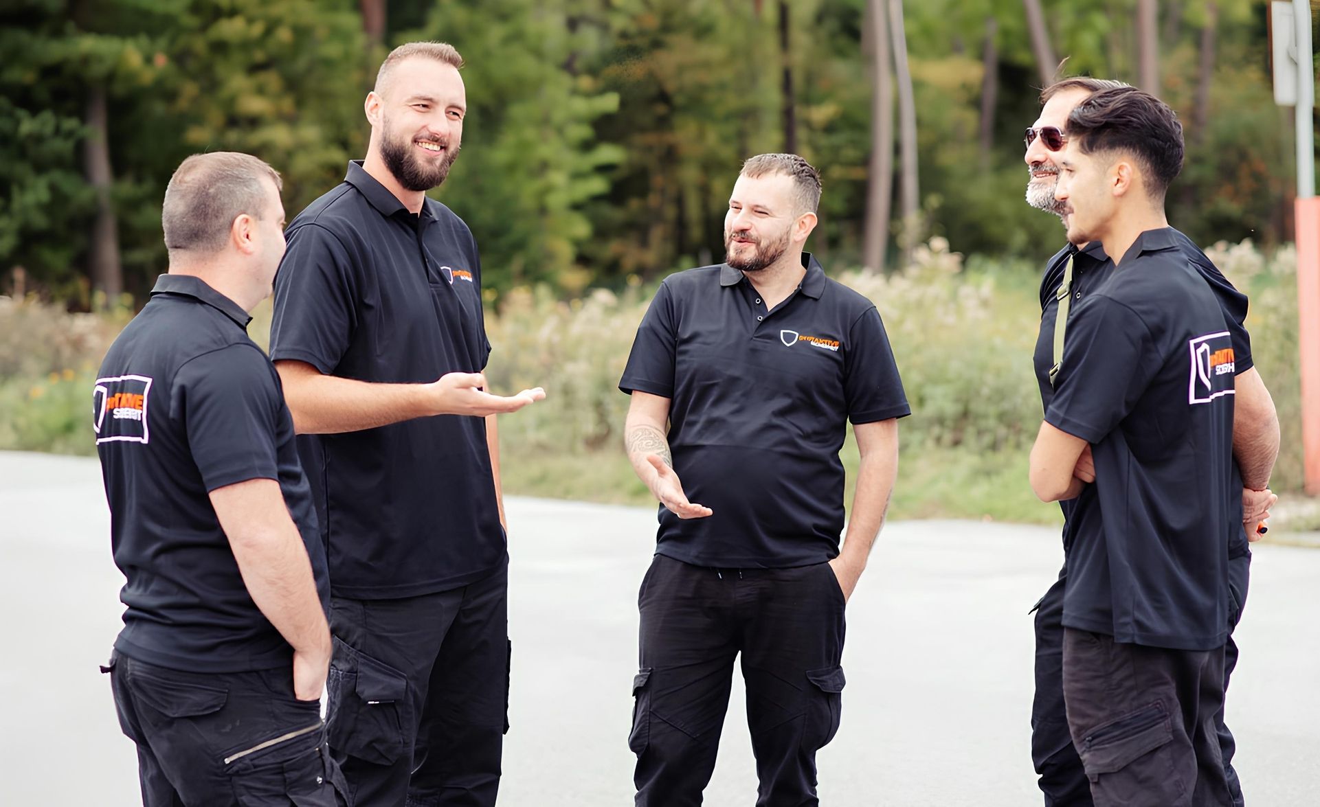 Vier Männer in schwarzer Arbeitskleidung stehen im Freien und unterhalten sich in lockerer Haltung